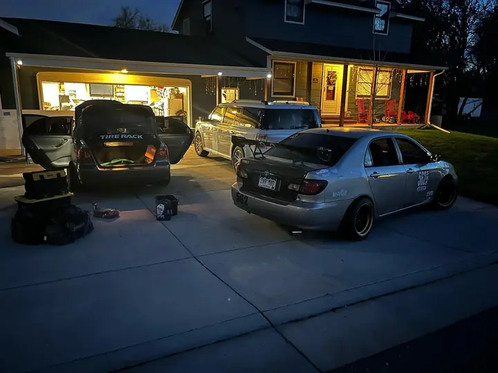 Two gray Dadbod Carmod Toyota Corollas parked outside a lit garage at night