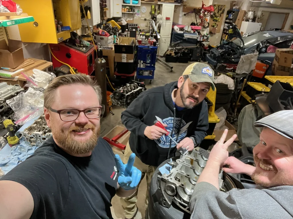 Three Dadbod Carmod team members working together on an engine in the garage